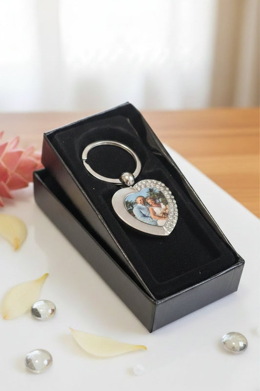 Heart-shaped keychain with a design in a black box on a light surface with petals.
