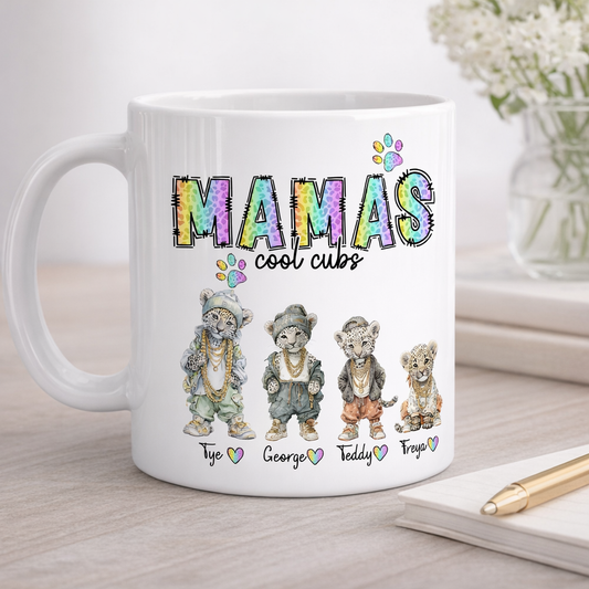White mug with colorful text 'Mamas cool cubs' and illustrations of four bears on a wooden surface.